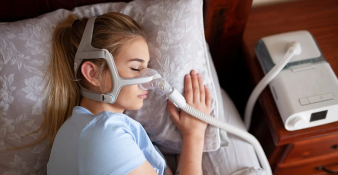 Mulher dormindo com o CPAP Automático DreamStation com Umidificador e máscara nasal Wisp